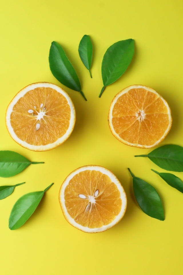 Половинки апельсина с зелеными листьями на желтом фоне