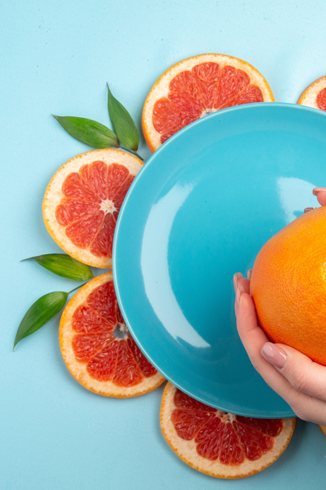 Апельсин в руках девушки на голубом фоне с тарелкой