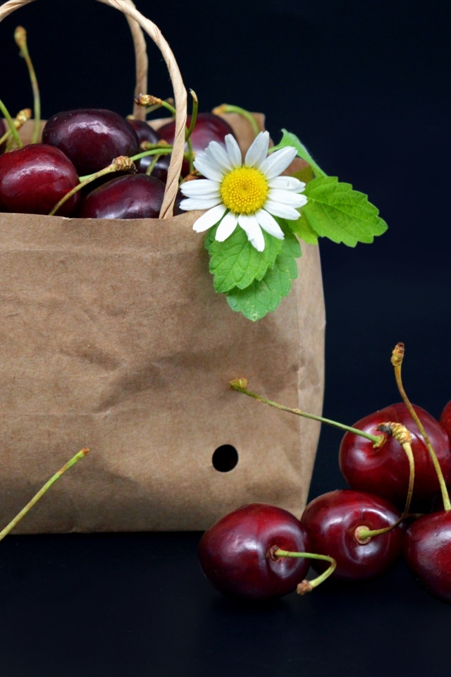 Бумажный пакет с ягодами черешни на черном фоне