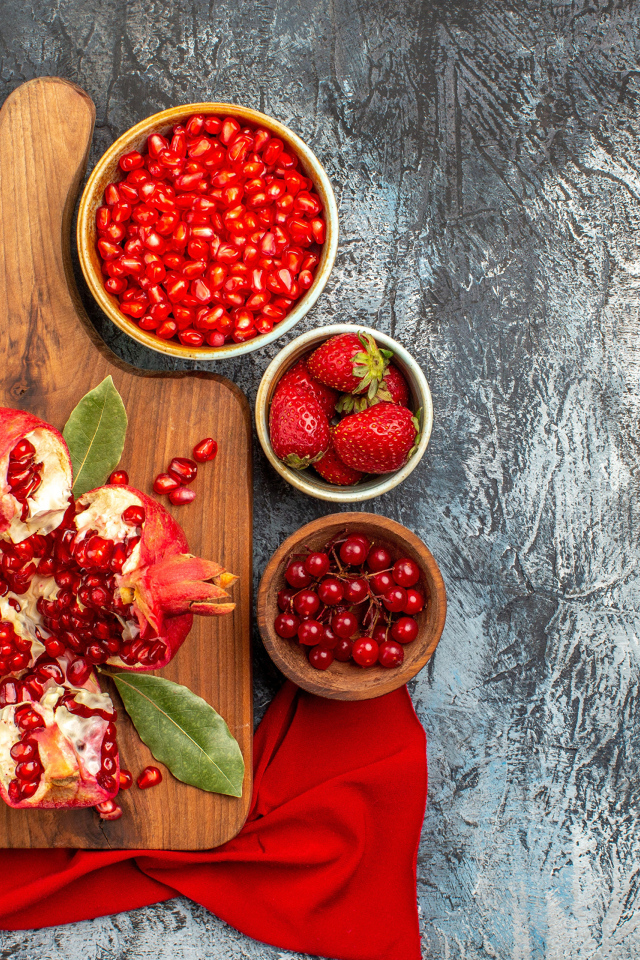 Очищенный гранат на столе с клубникой и ягодами смородины