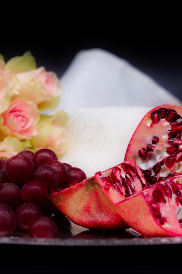 Гранат с виноградом на столе с букетом роз 