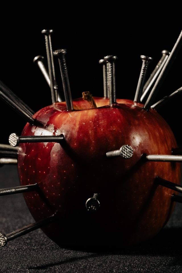 Красное яблоко с гвоздями на черном фоне