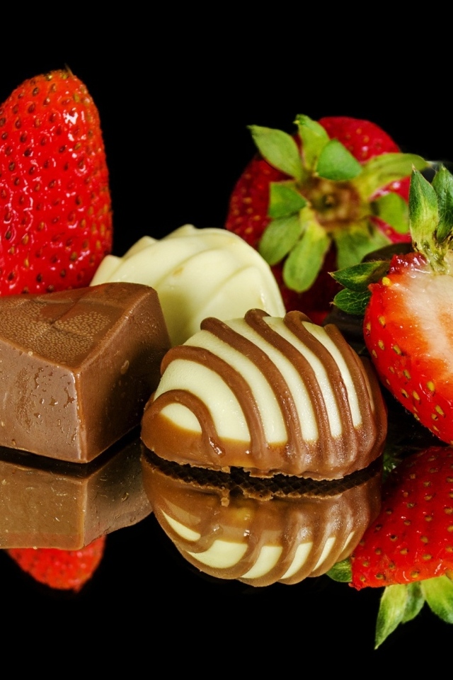 Красная клубника с шоколадными конфетами на черном фоне