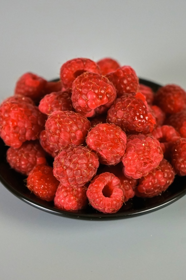 Спелая красная малина в черной тарелке на сером фоне