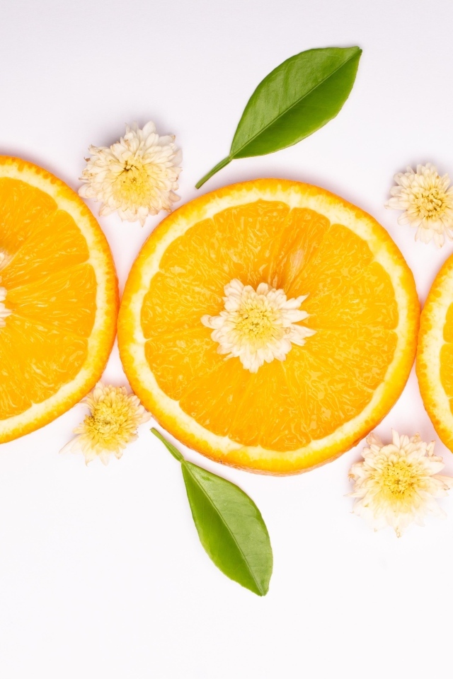 Три кружочка апельсина на белом фоне с цветами и зелеными листьями