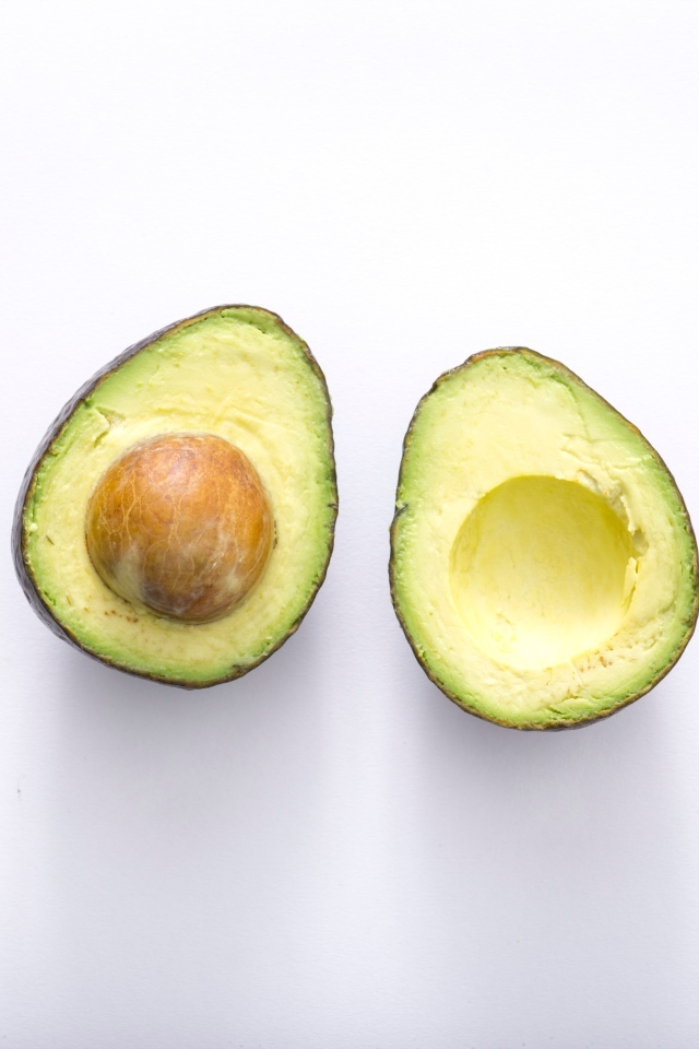 Две половинки зеленого авокадо на сером фоне