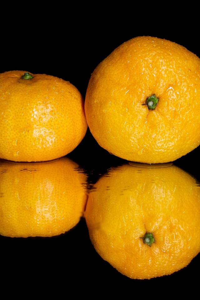 Два мандарина на черной зеркальной поверхности 