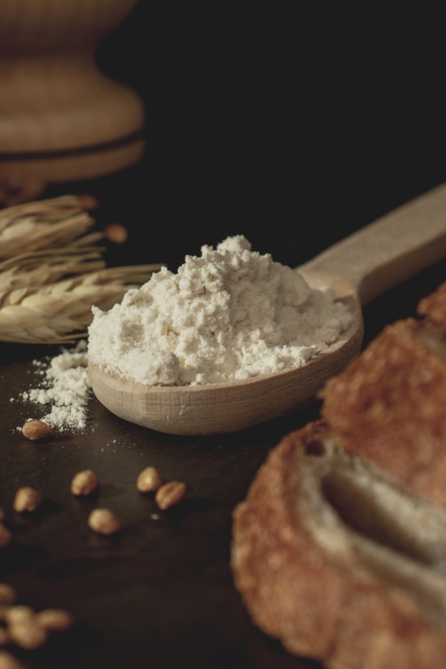 Ложка муки на столе с пшеницей и хлебом
