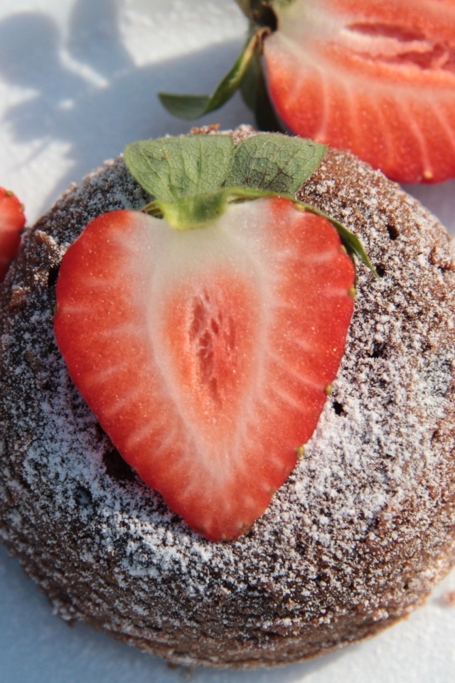 Пирожное на  тарелке с клубникой и сахарной пудрой