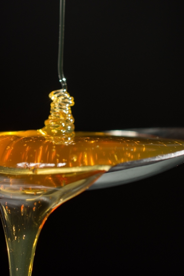 Мед наливают в ложку на черном фоне