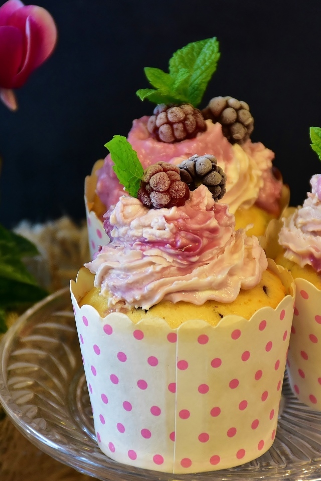 Маффины с кремом и ягодами малины на столе с цветами