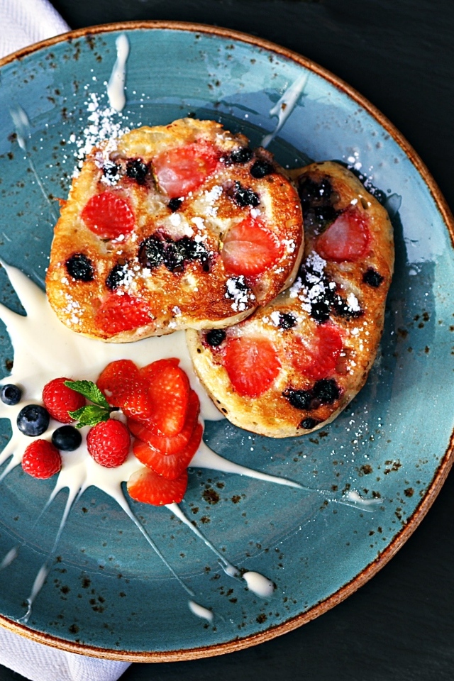 Оладьи на тарелке с ягодами и сметаной