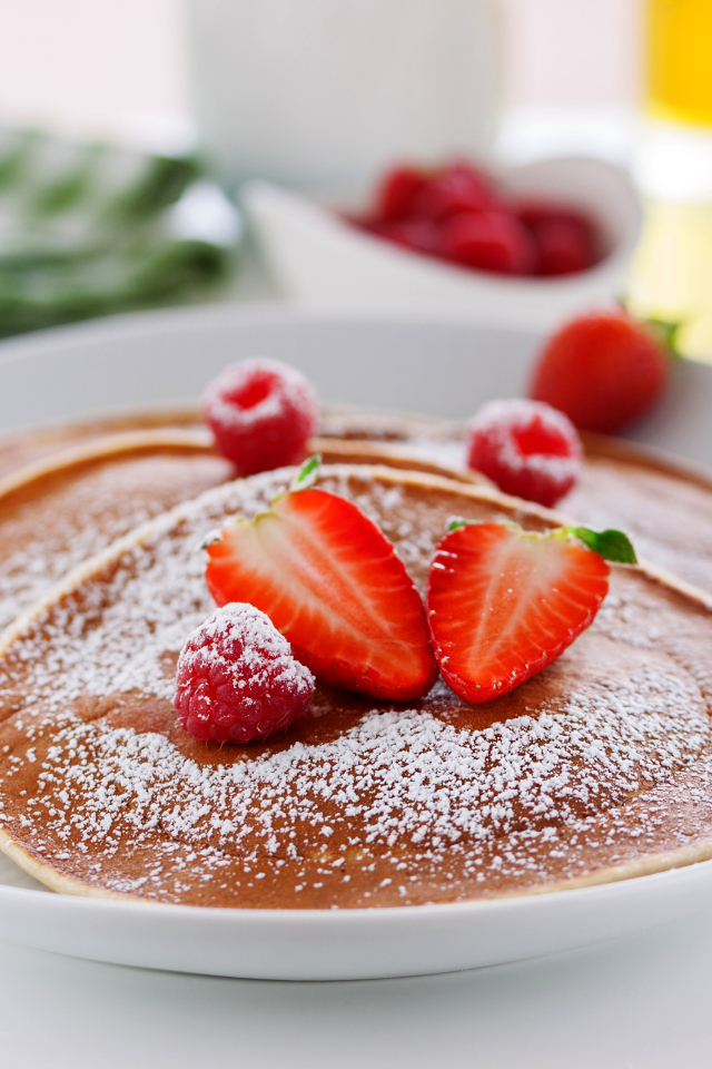 Оладьи на тарелке с сахарной пудрой и ягодами клубники