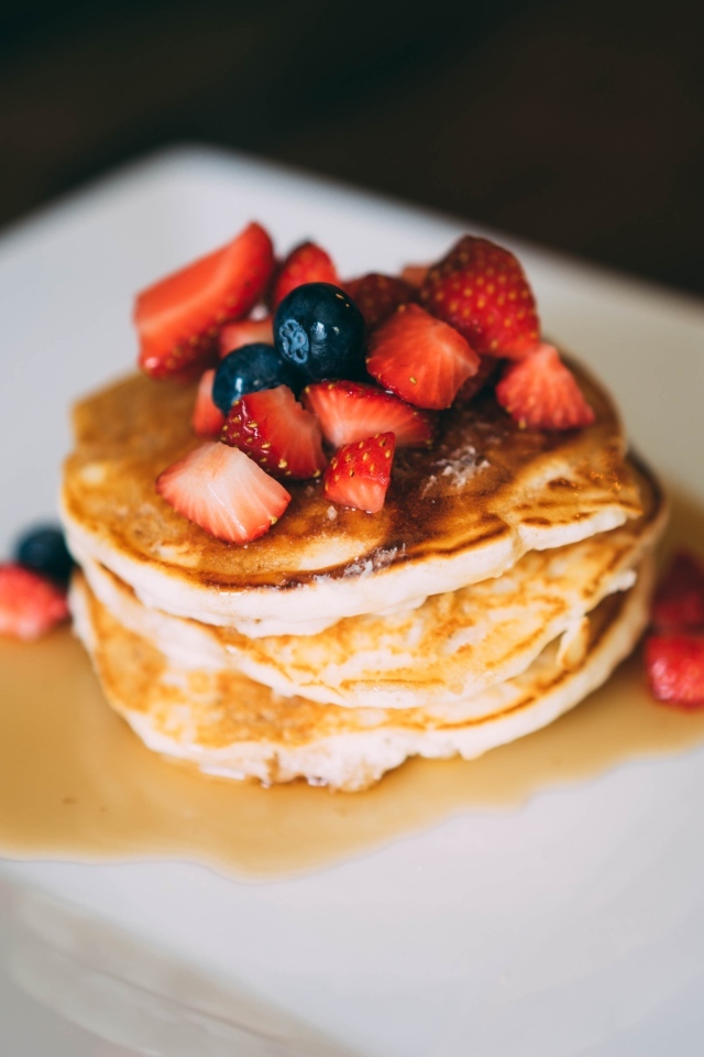 Оладьи с кусочками клубники, медом и черникой на тарелке