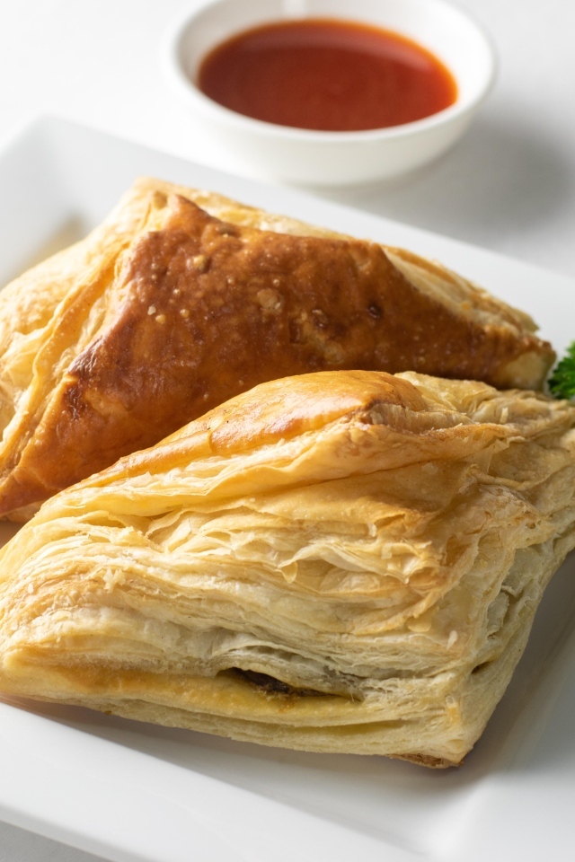 Слоеная выпечка на белой тарелке с соусом