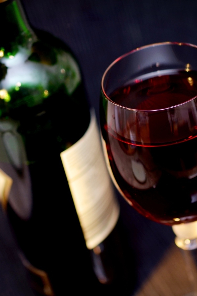 Бутылка красного вина с бокалом на столе