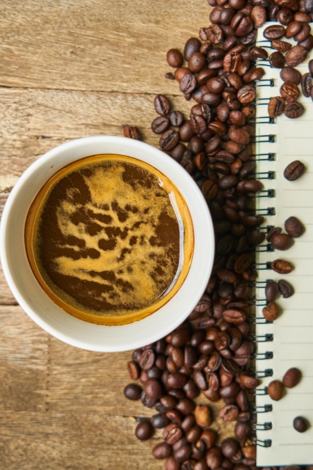 Чашка кофе на столе с зернами и блокнотом