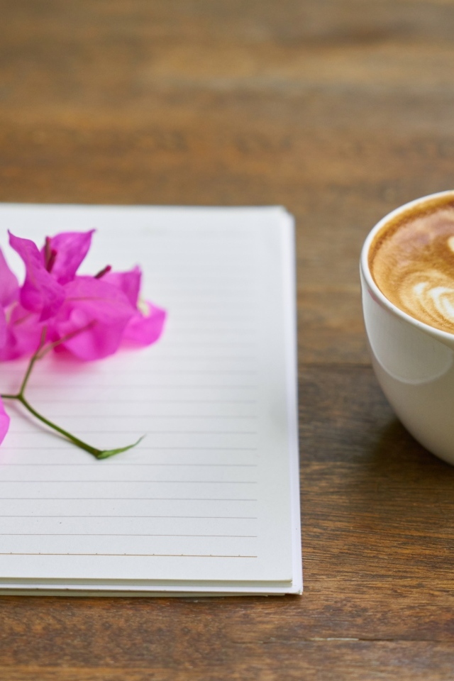 Чашка кофе на столе с блокнотом и цветами