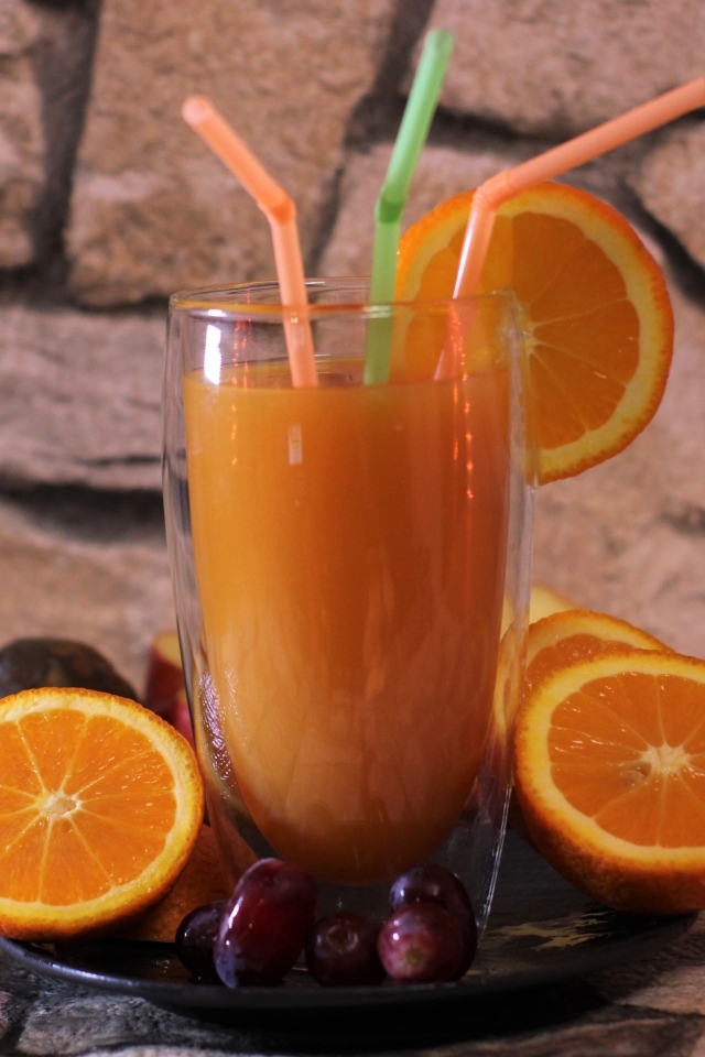 Стакан свежего сока с трубочками на столе с апельсинами