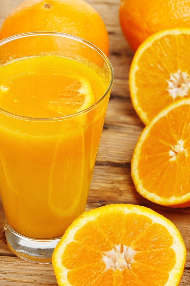 Стакан свежевыжатого сока на столе с половинками апельсина