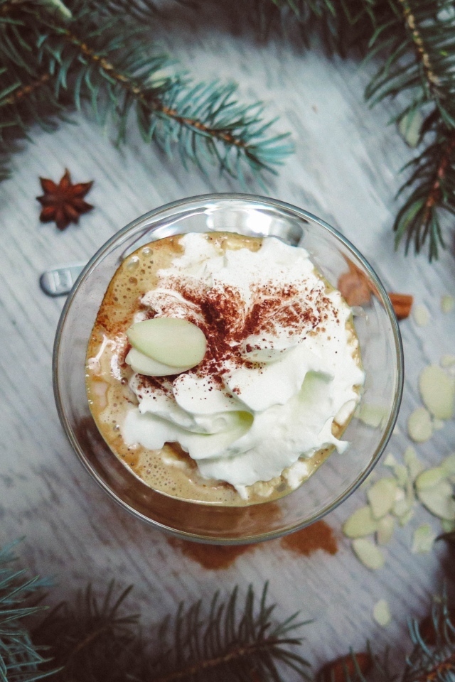 Горячий кофе с взбитыми сливками в чашке на столе с еловыми ветками