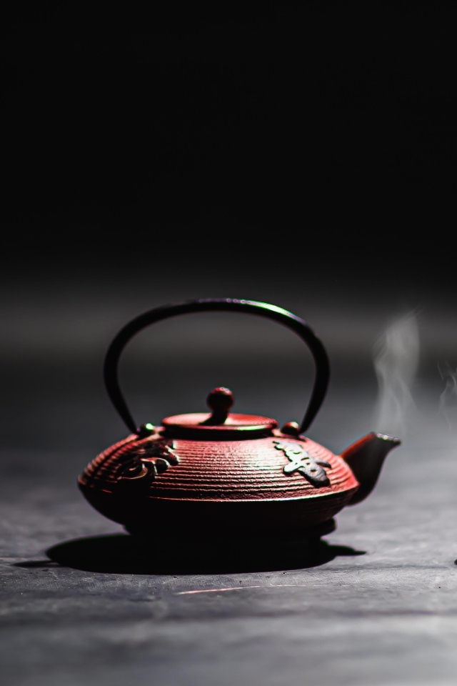 Чайник с горячим чаем на черном фоне