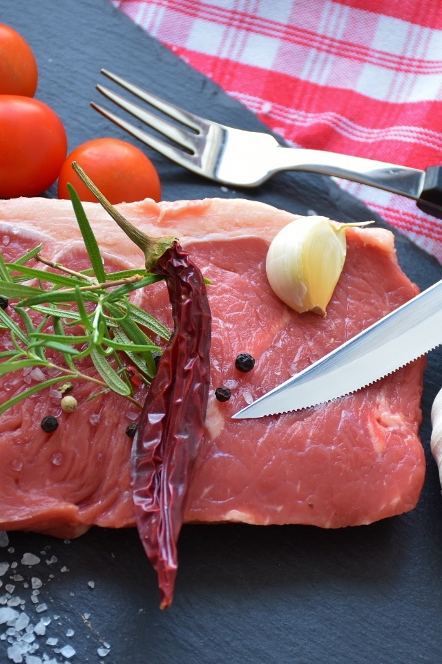 Большой кусок свинины на столе с чесноком и помидорами