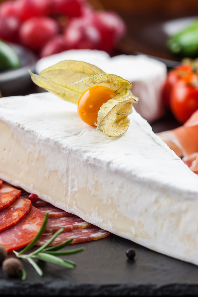 Кусок сыра на столе с овощами и колбасой