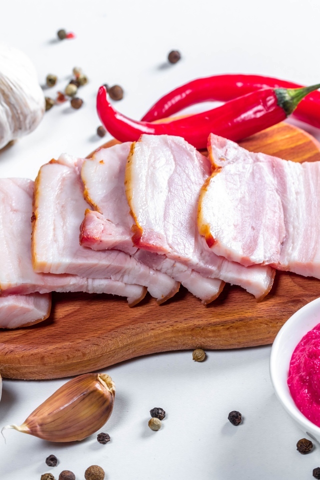 Нарезанное сало на столе с чесноком, хреном и красным перцем