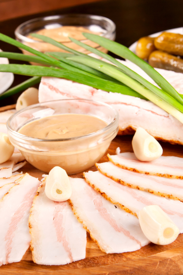 Нарезанное сало с чесноком и солеными огурцами на столе