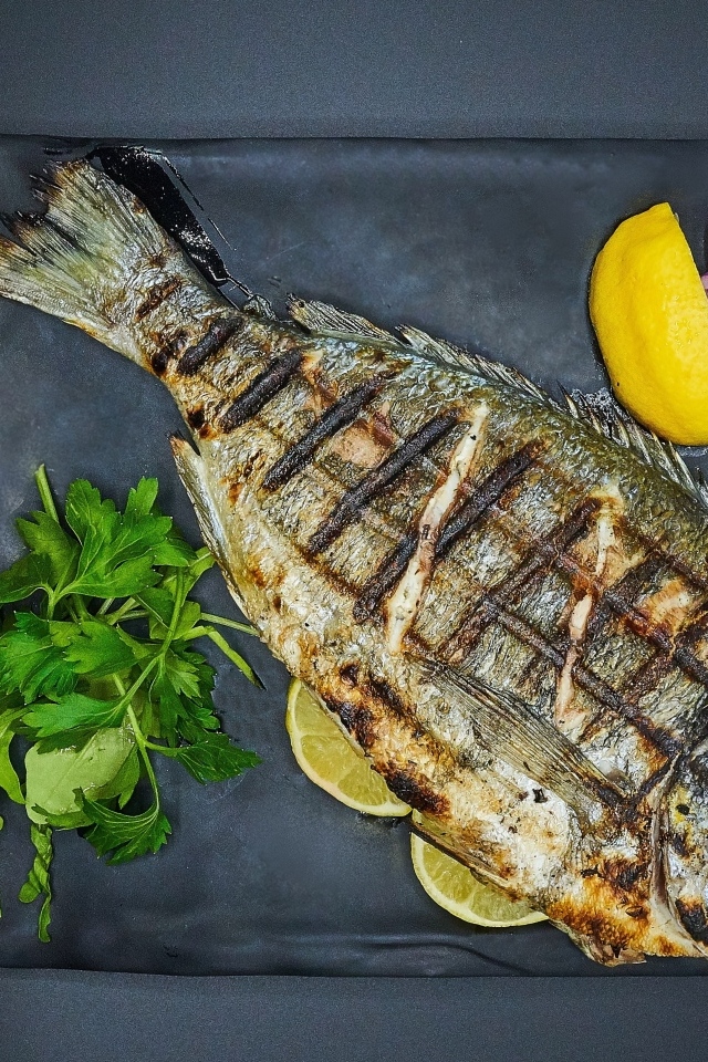 Жареная рыба с лимоном, луком и петрушкой на тарелке