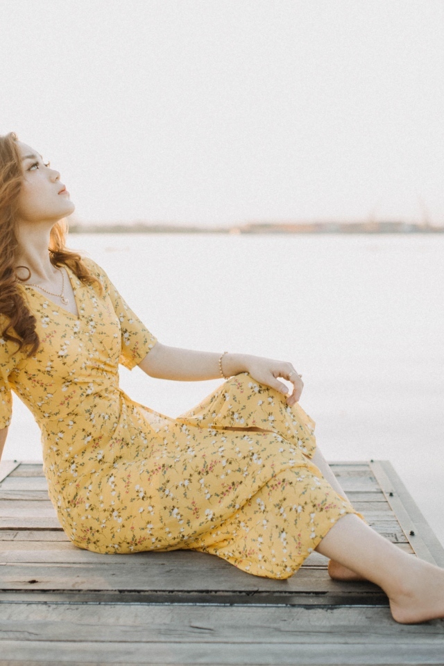 Красивая девушка в платье сидит на мосту у реки