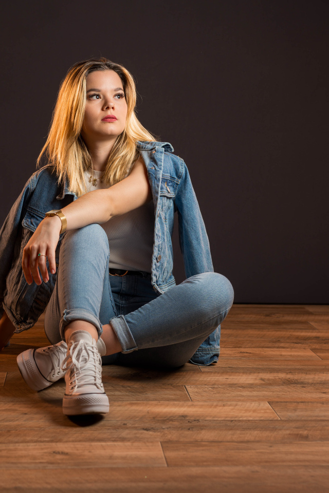 Девушка в джинсовом костюме сидит на полу