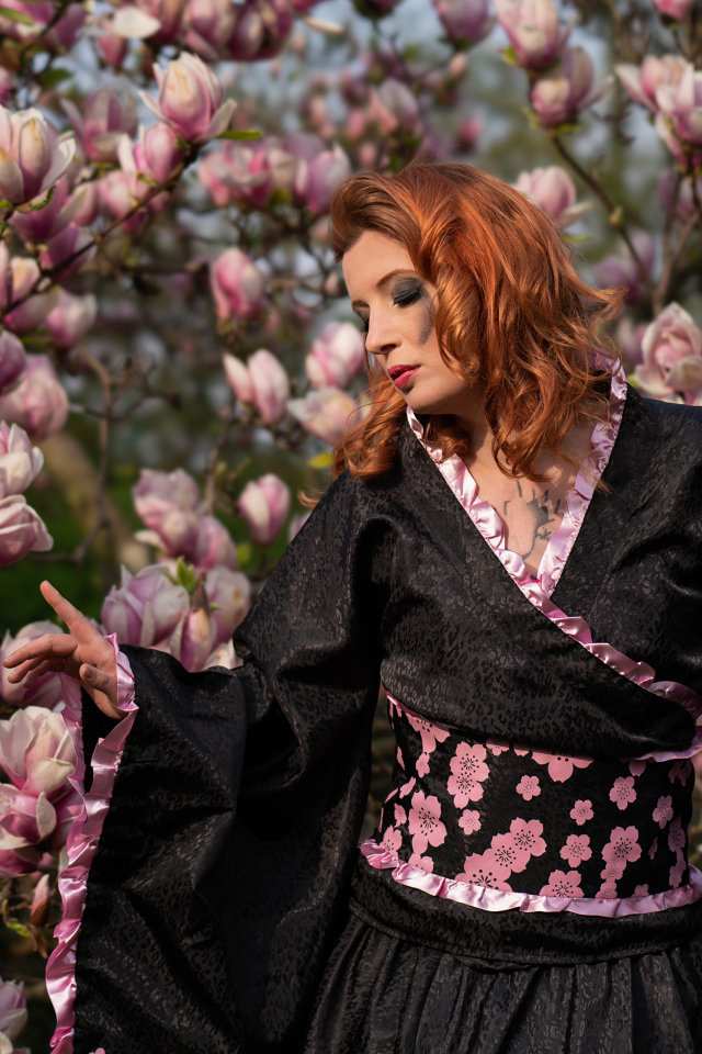 Девушка в кимоно стоит у куста с цветами магнолии