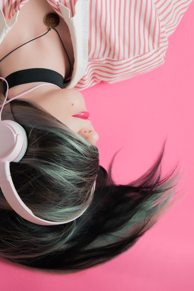 Девушка в наушниках лежит на розовом полу