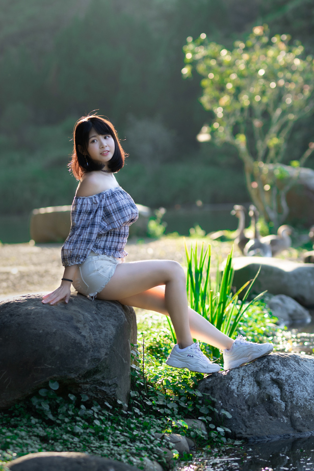 Девушка сидит на большом камне у пруда