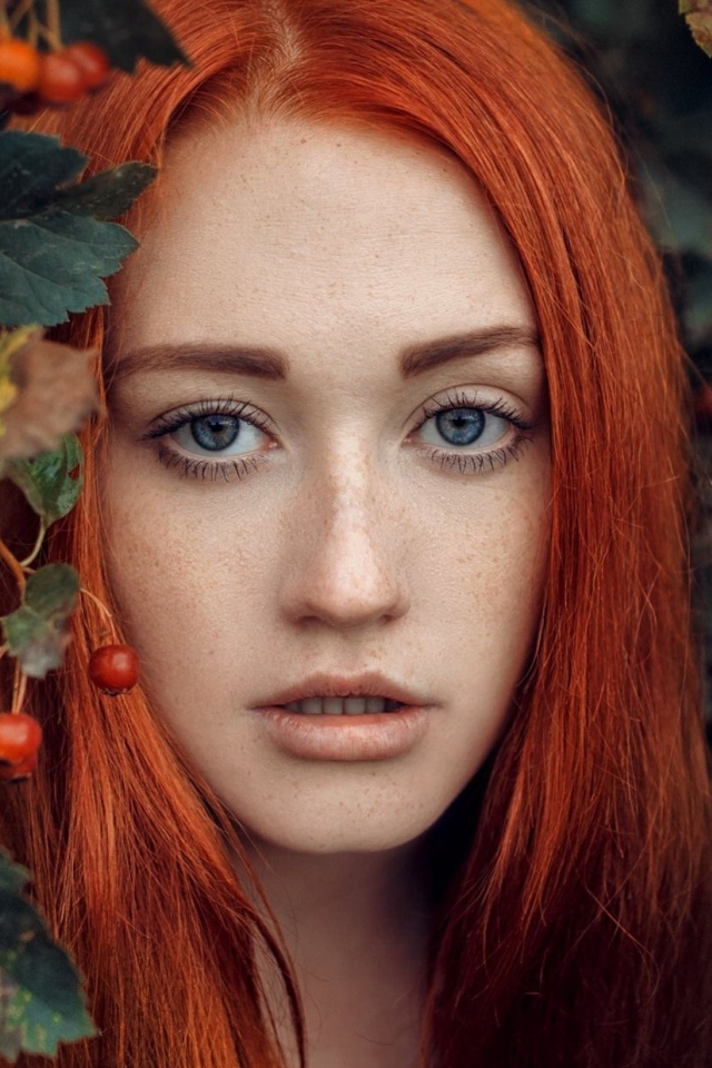 Рыжеволосая девушка стоит у куста с боярышником