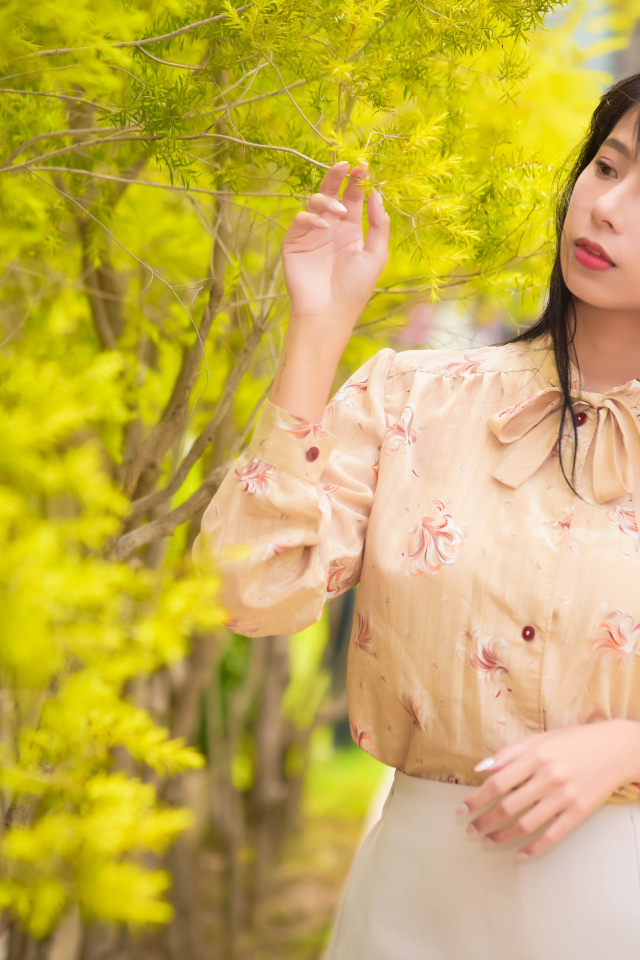 Молодая девушка азиатка стоит у дерева с зелеными листьями