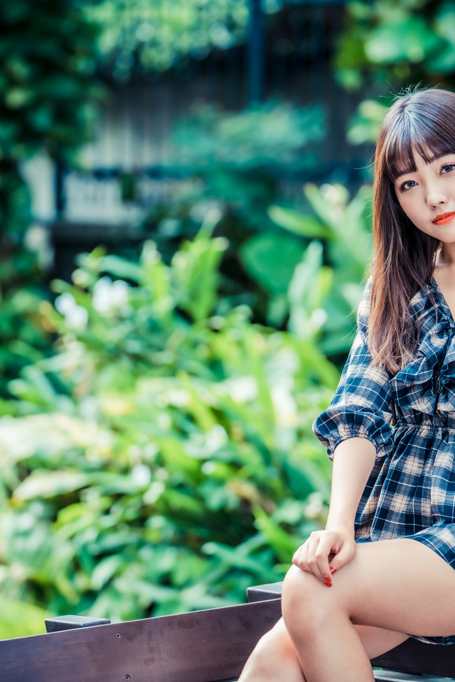 Молодая девушка в клетчатом платье сидит на заборе