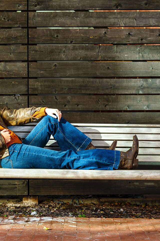 Молодая девушка в синих джинсах лежит на лавке