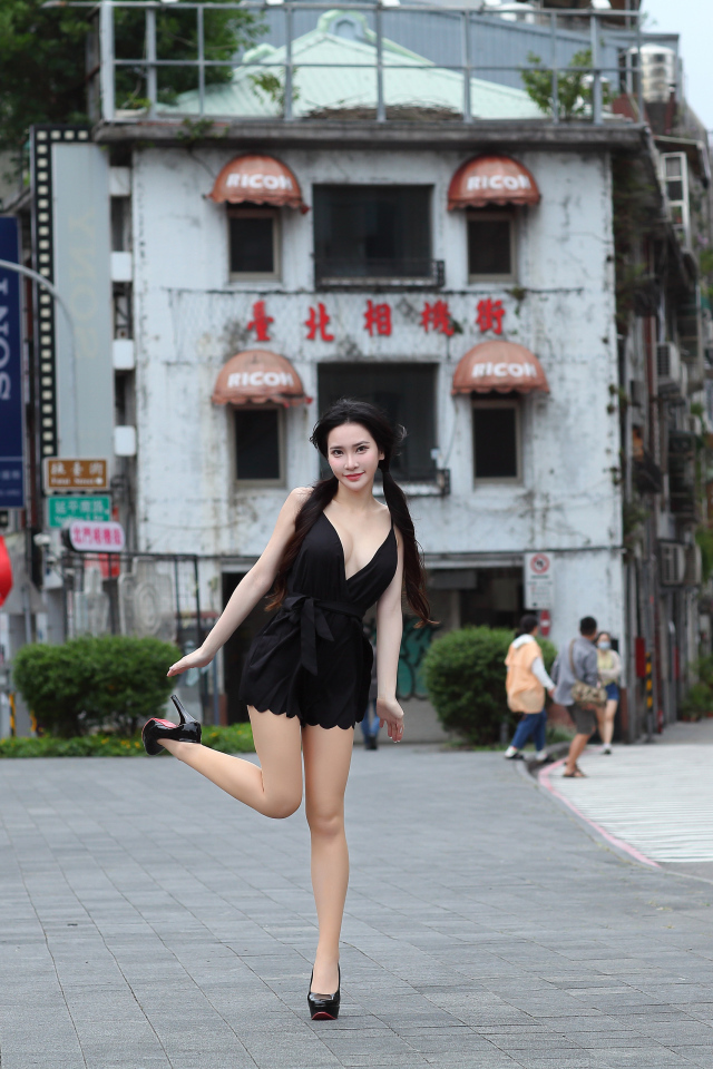 Девушка азиатка в черном платье стоит у дома