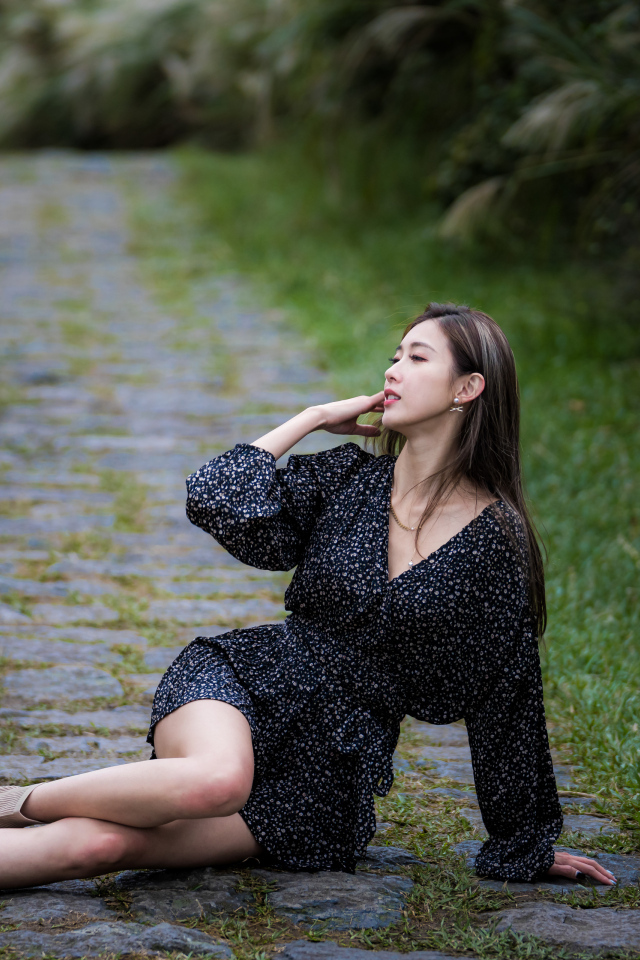 Девушка азиатка в платье лежит на дороге в парке