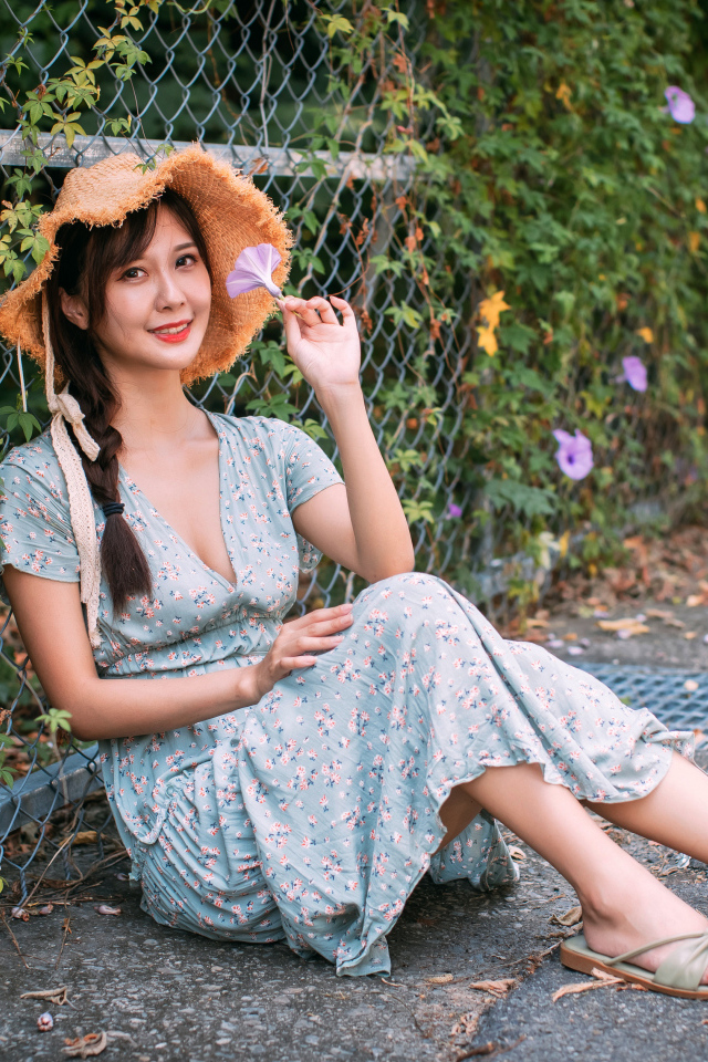 Девушка азиатка в платье сидит у забора