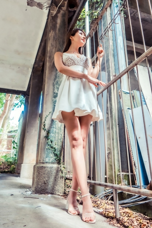 Девушка азиатка в платье стоит у решетки 