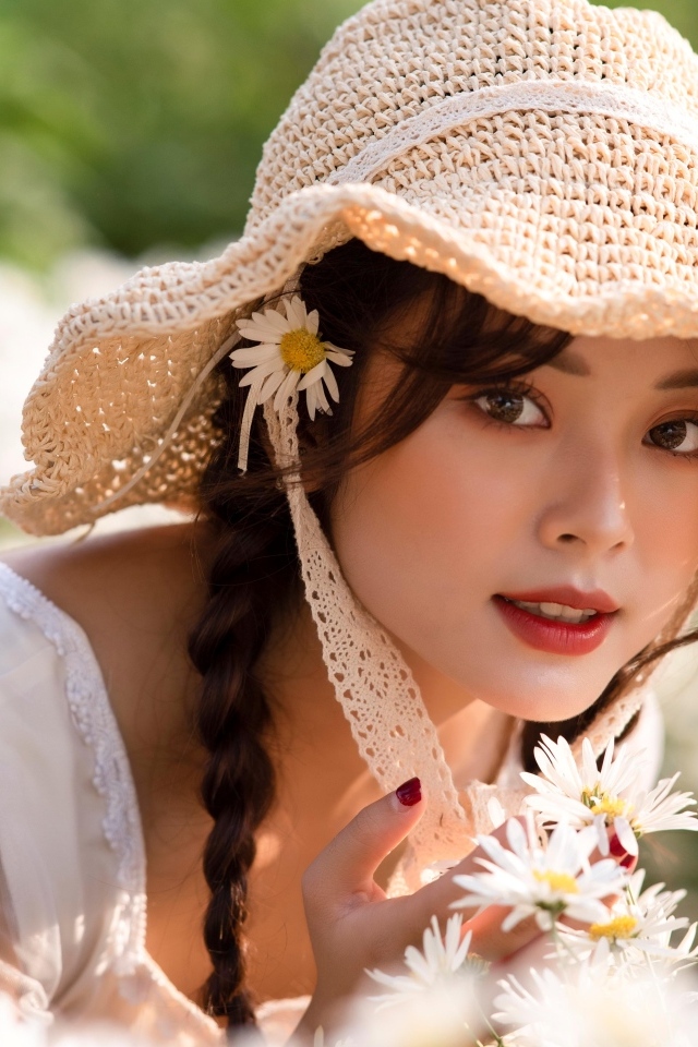 Девушка азиатка в шляпке на поле с ромашками