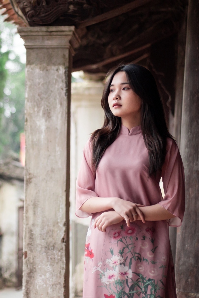 Девушка азиатка в розовом платье стоит у дома