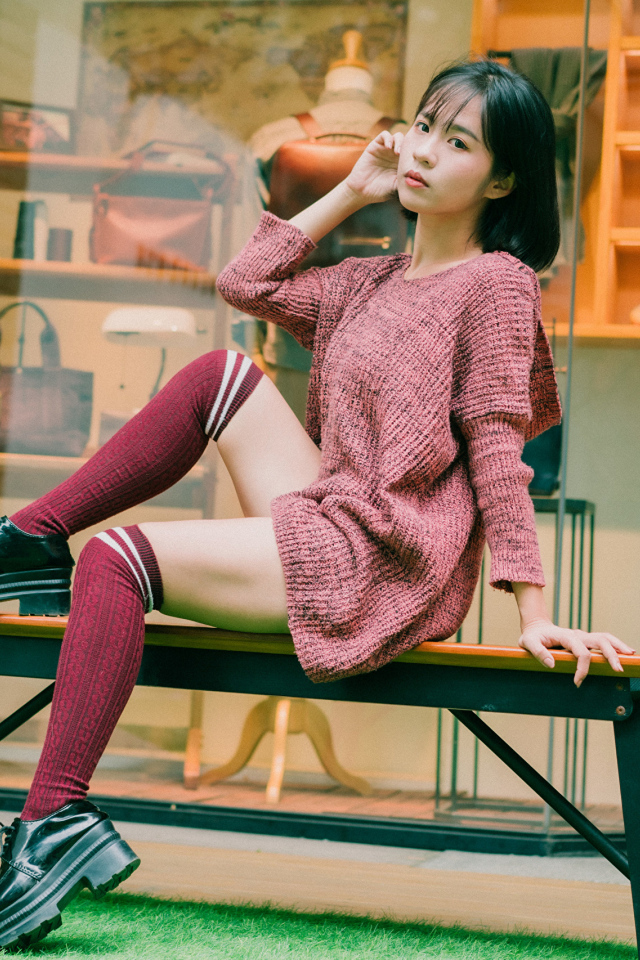 Девушка азиатка в теплом свитере сидит на лавке