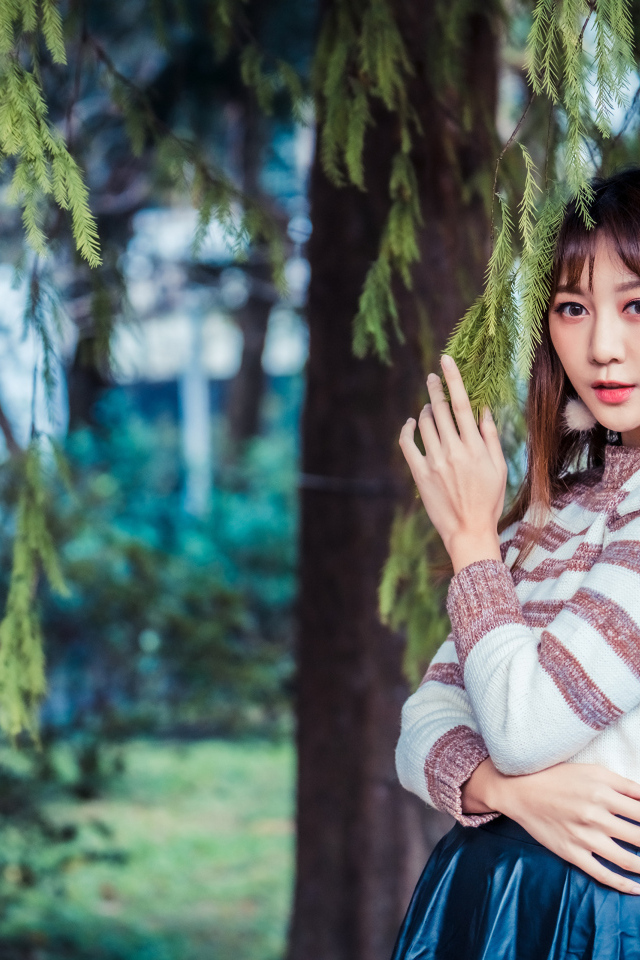 Девушка азиатка стоит у дерева ели