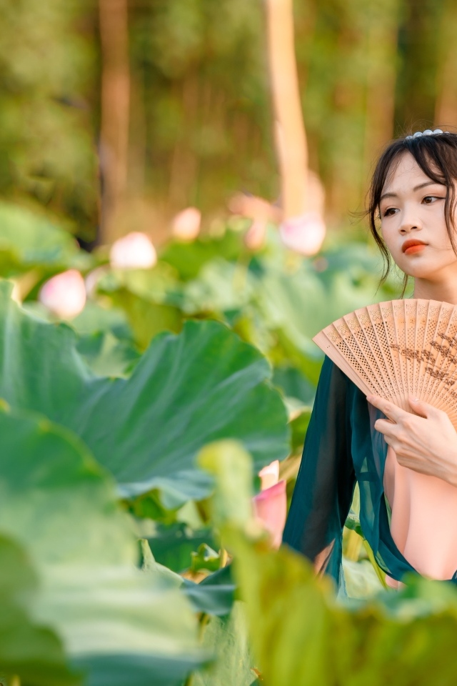 Девушка азиатка с веером в зеленых листьях лотоса
