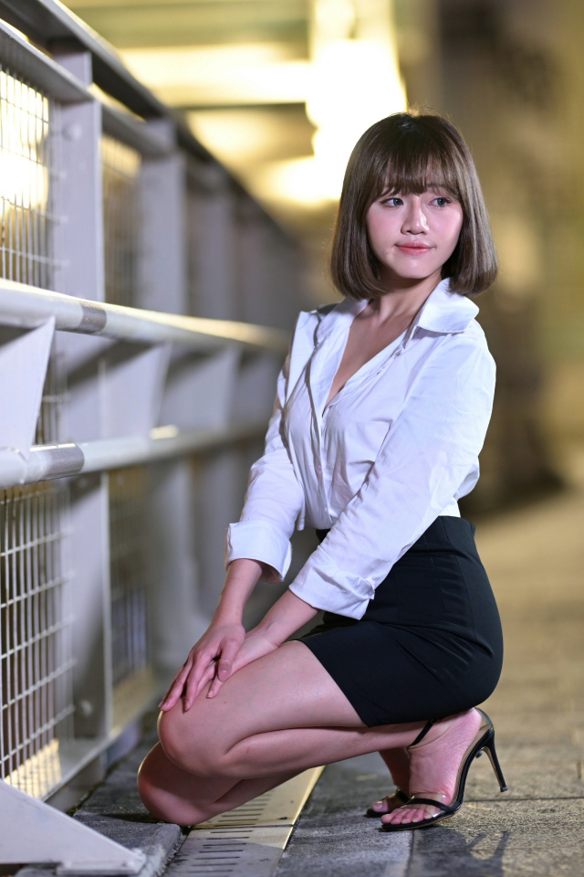 Азиатка в белой блузке и черной юбке сидит на корточках